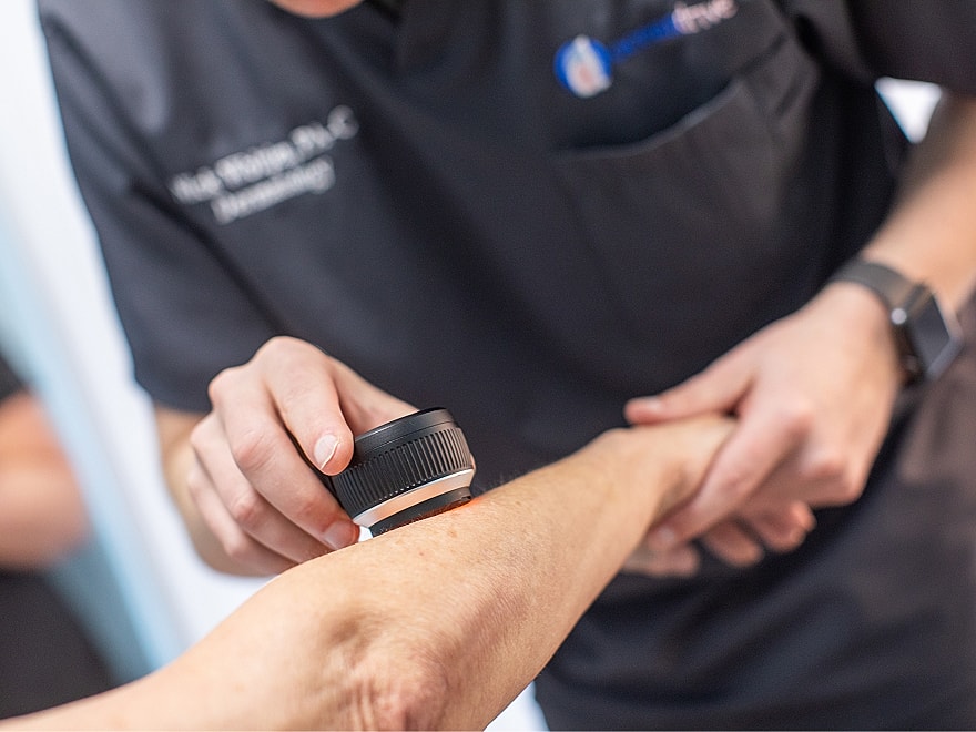Medical professional examining skin with handheld device.