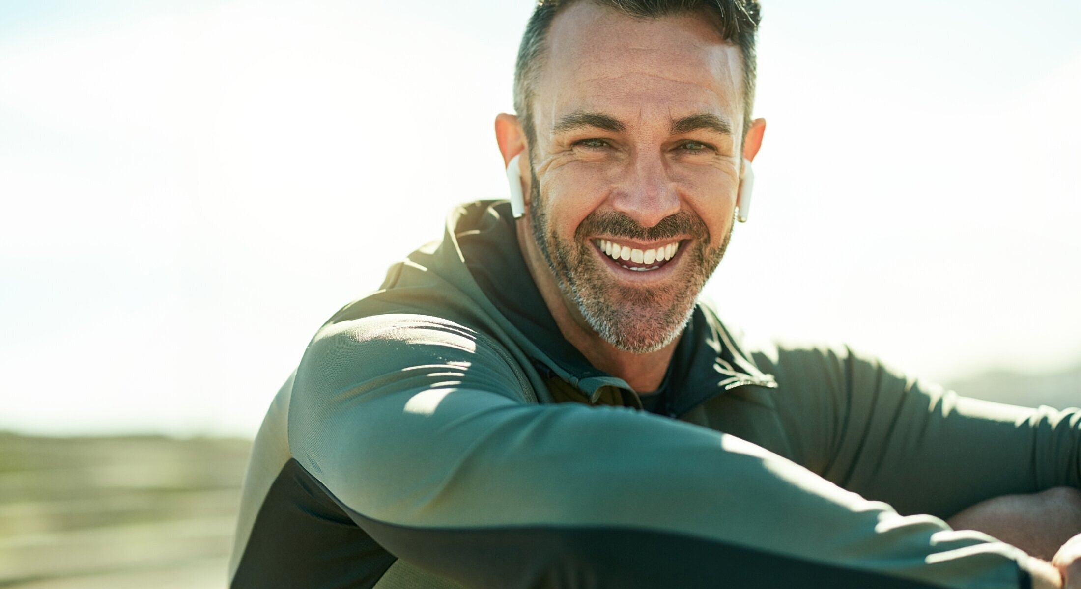 Smiling man in athletic wear outdoors with earbuds.